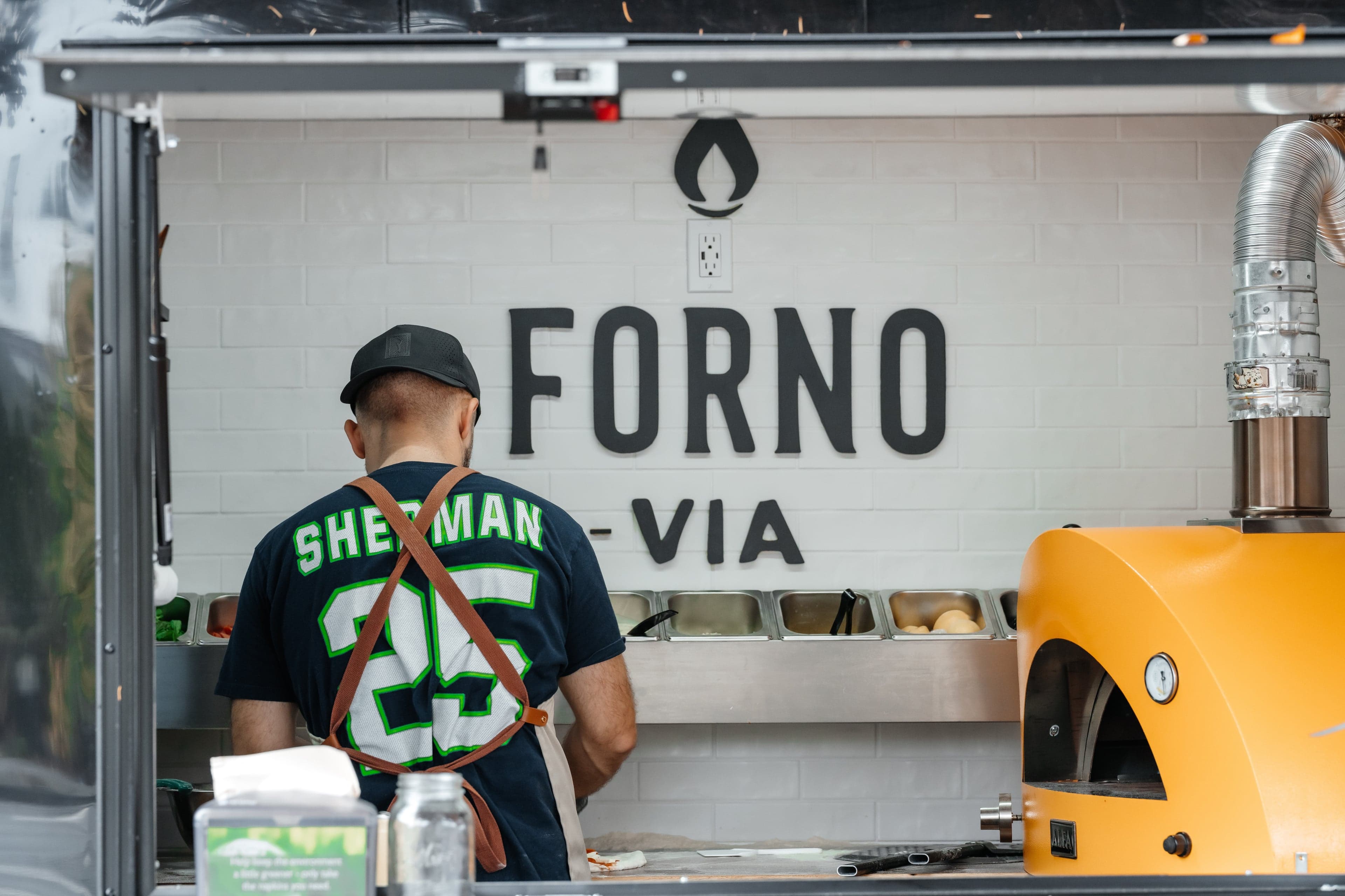 Forno Via mobile wood-fired pizza trailer catering a Seattle outdoor event with flames visible in the oven