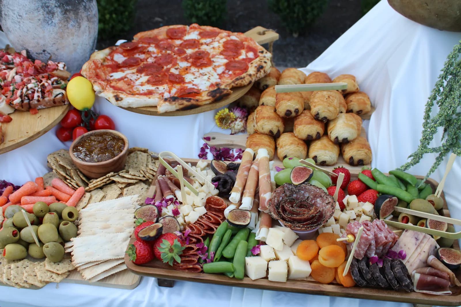 Grazing table spread with pizza, cured meats, cheeses, vegetables, fruit, and crackers