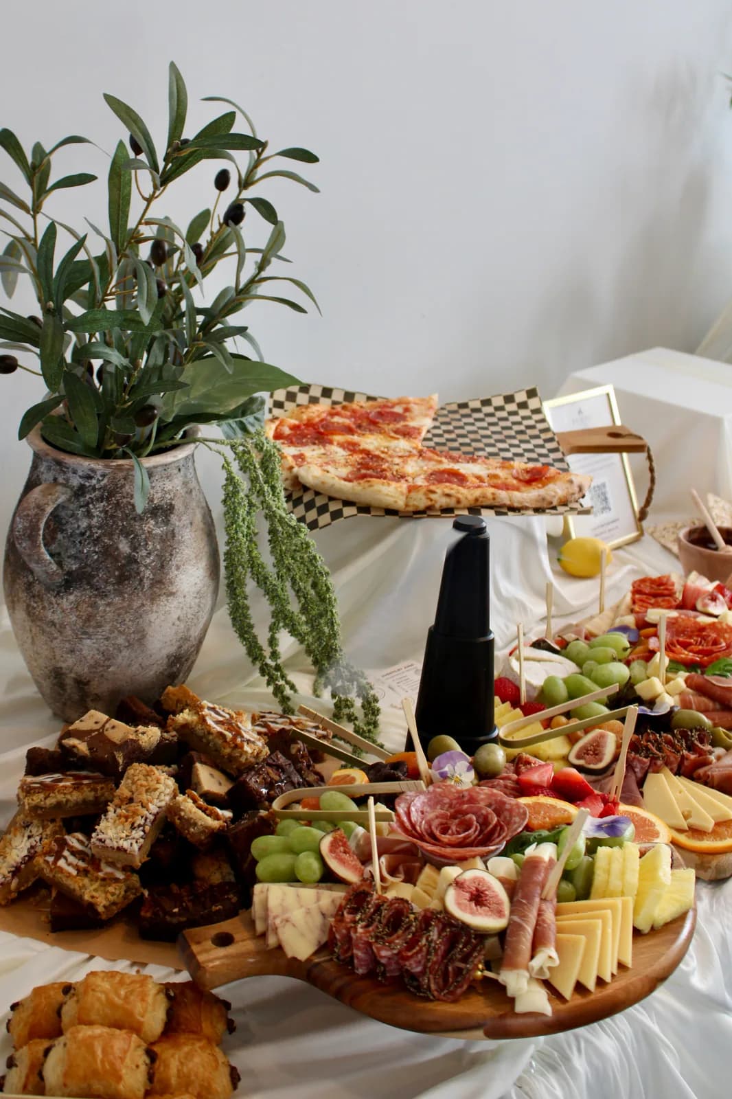 Indoor Forno Via grazing table with charcuterie boards, pizza, breads, and greenery